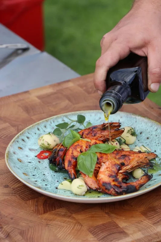 Riesengarnelen Mit Olivenöl Mietkoch Chris verfeinert gegrillte Riesengarnelen mit Olivenöl auf blauem Teller.