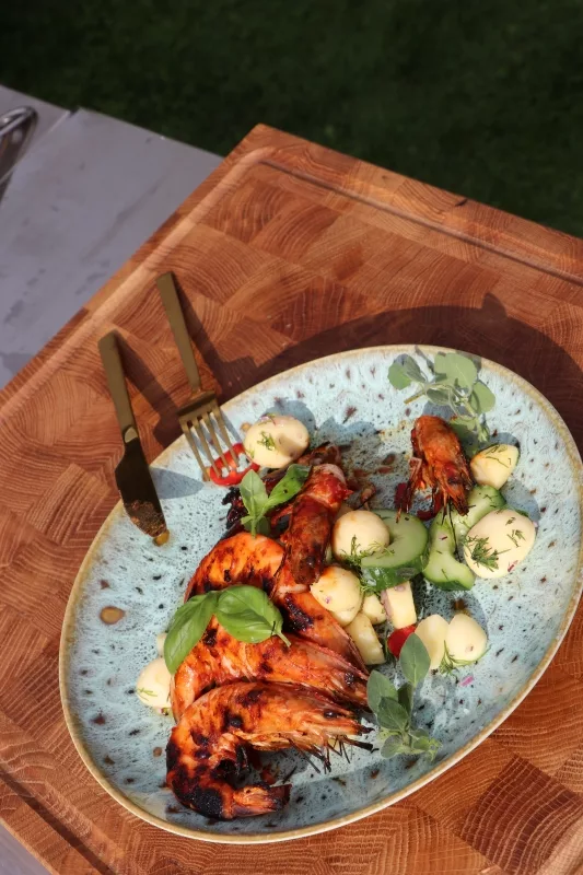 Exklusiver Seafood Meze Teller Das fertige maritime Meze-Gericht mit perfekt gegrillten Riesengarnelen, frischen Gurken und Kräutern serviert im Garten.